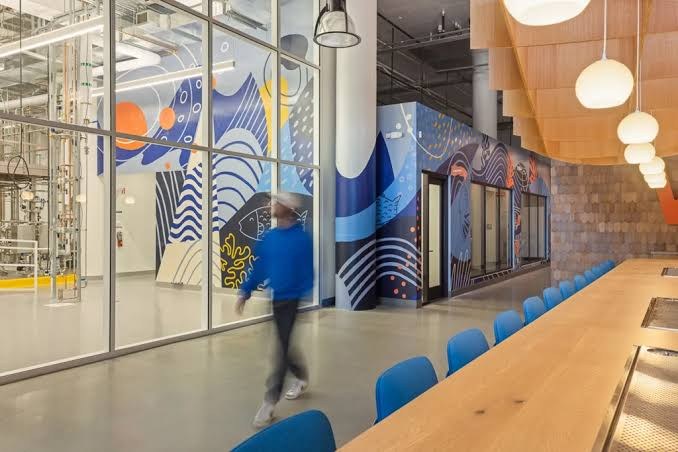 Inside Wildtype's fishery: a glass-walled production floor beside a mural of fish and waves.