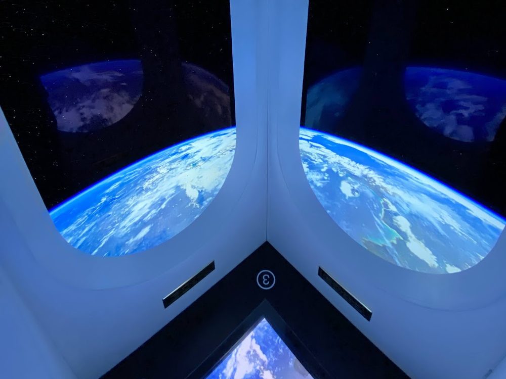 Inside a spacecraft simulator, two tall windows looking down on the curve of the Earth.
