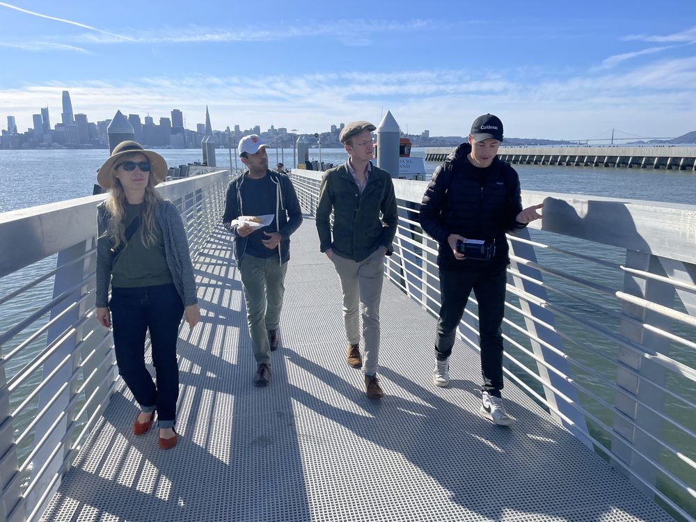 Four people walking a pier toward the San Francisco skyline on a World's Fair Co. tour.
